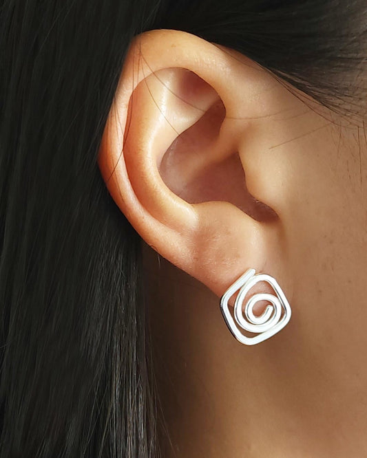 Close up of person with black hair wearing diamond-shaped silver stud earrings in swirl design