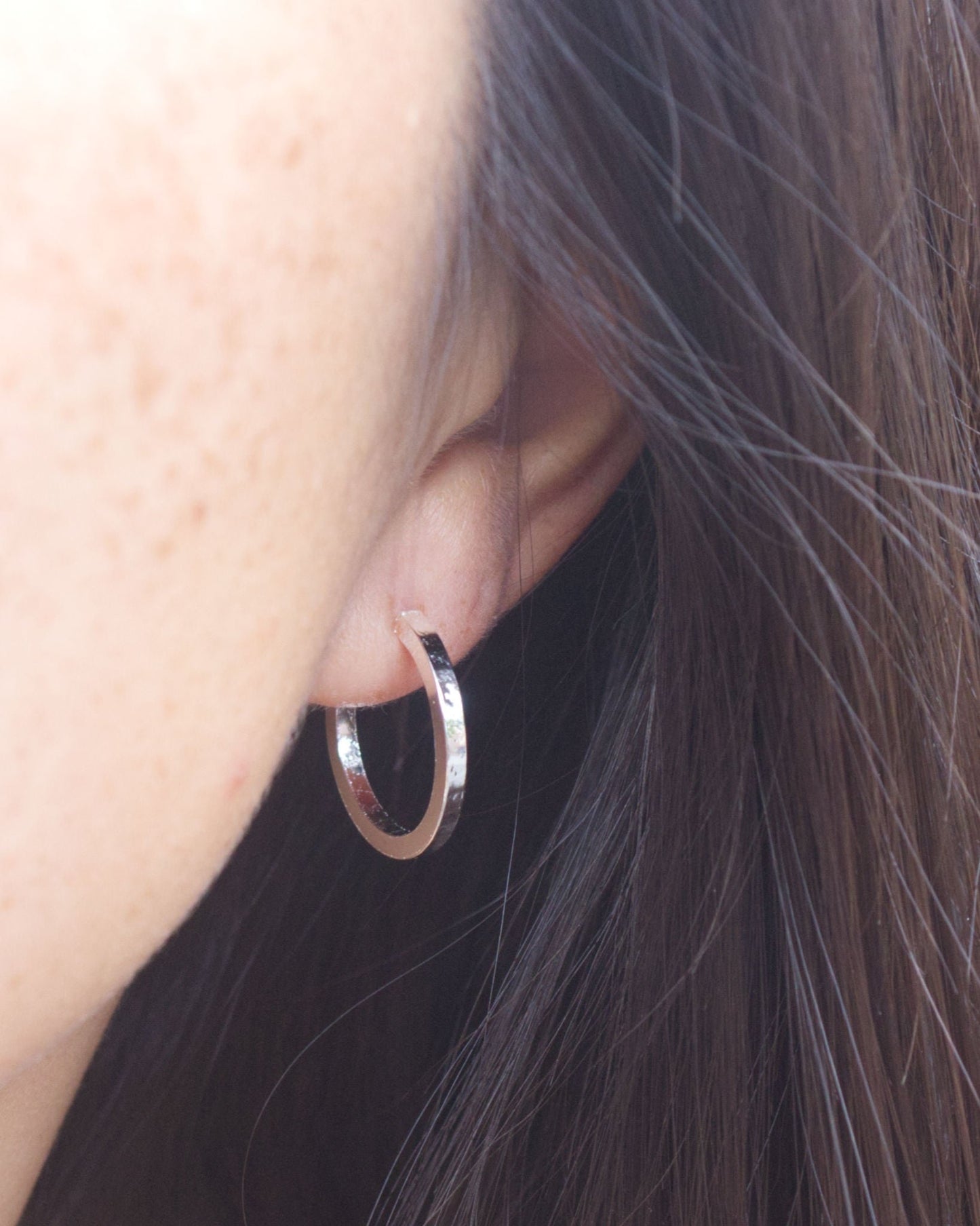 Close up of person wearing small silver hoop earrings with texture on front and back