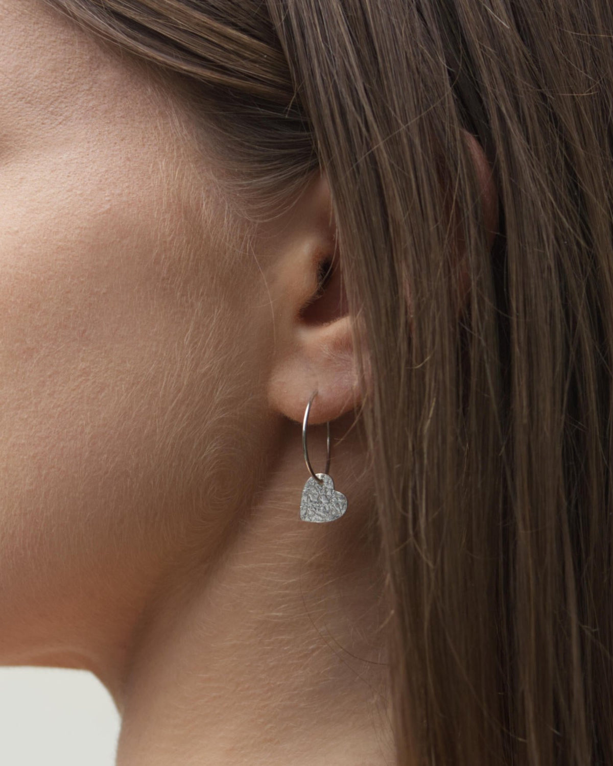 Side view of person wearing silver hoops with small textured hearts