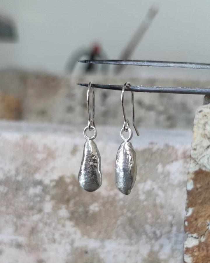 Elegant long molten silver earrings on handmade silver hooks being held in mid-air by jewellery tweezers