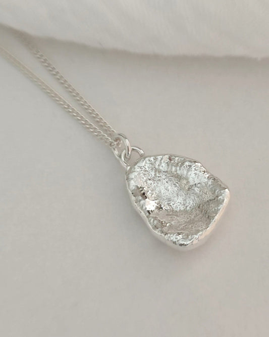 Back view of molten silver pendant with curved profile hanging from fine silver chain and lying on white background