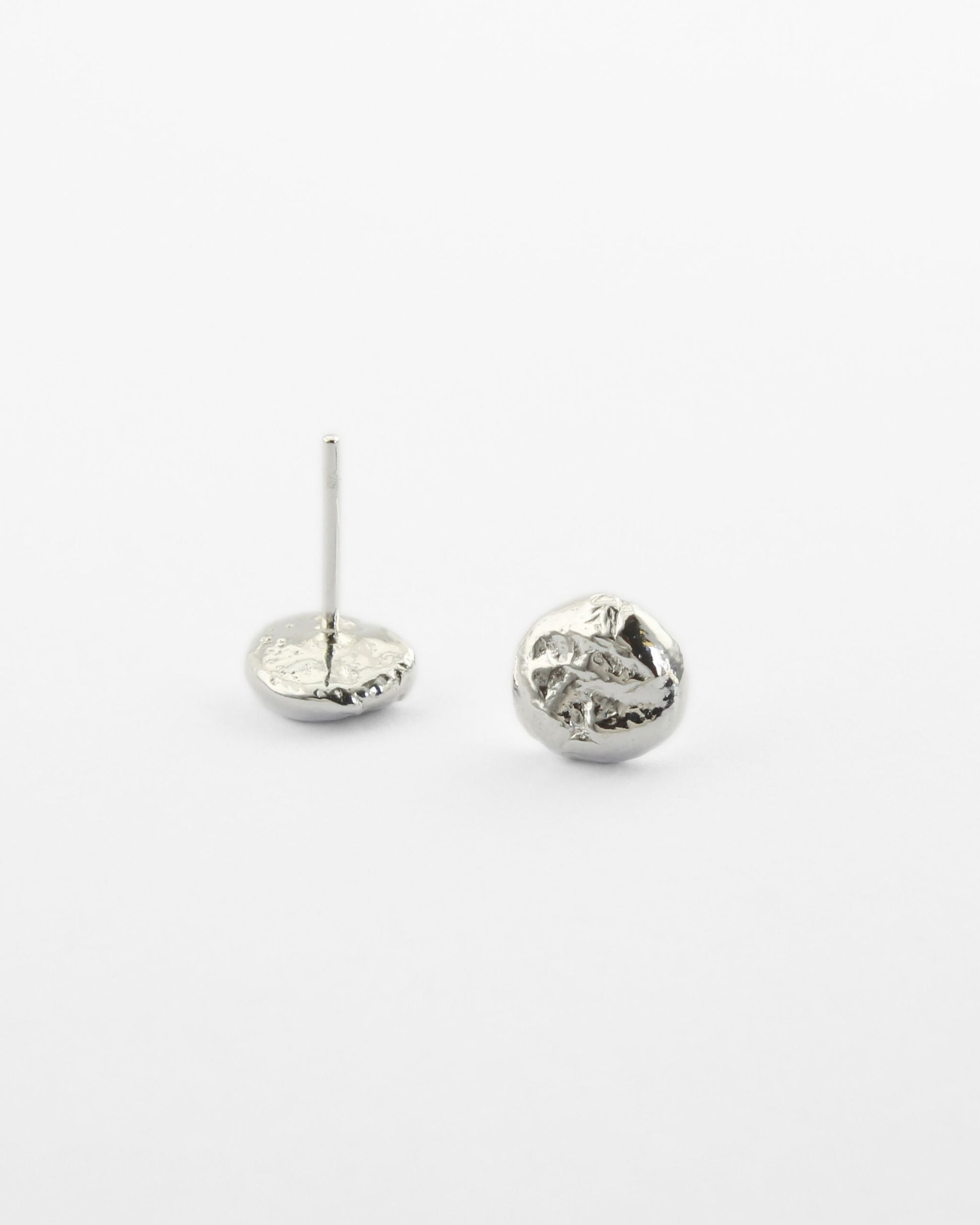 Small molten silver stud earrings with a delicate texture lying on off-white surface