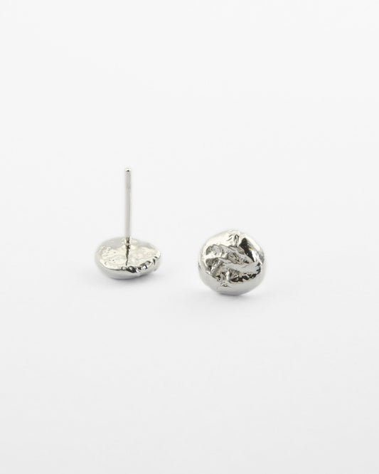 Small molten silver stud earrings with a delicate texture lying on off-white surface