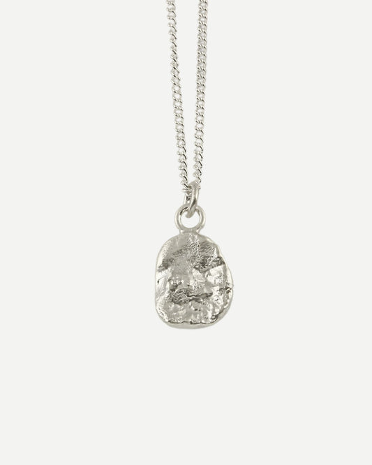 Back view of small molten silver pendant with organic textured surface hanging on fine curb chain on white background
