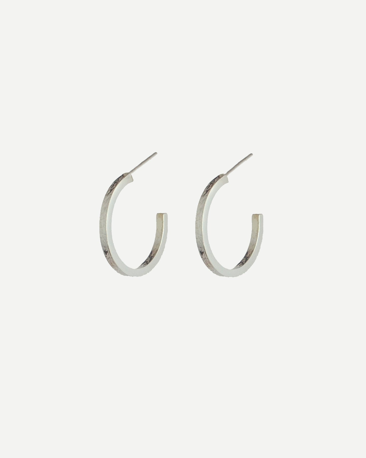 Silver hoop earrings with delicate texture on front and back, with off-white background