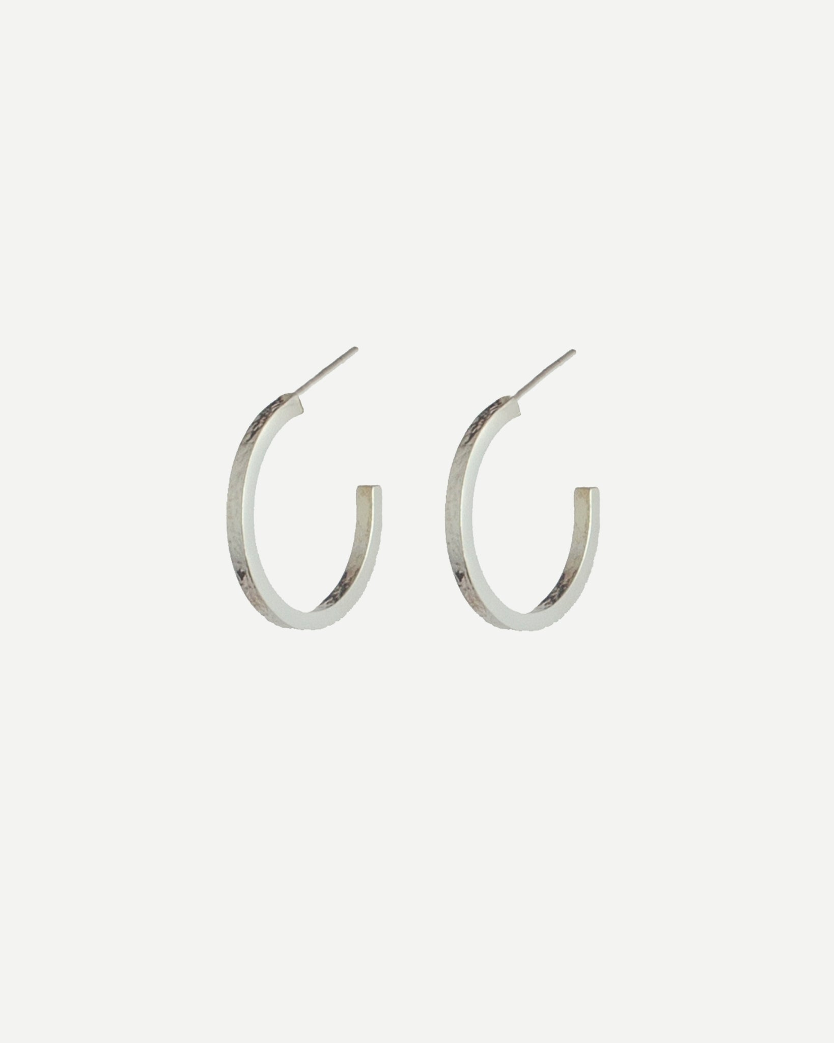 Silver hoop earrings with delicate texture on front and back, with off-white background
