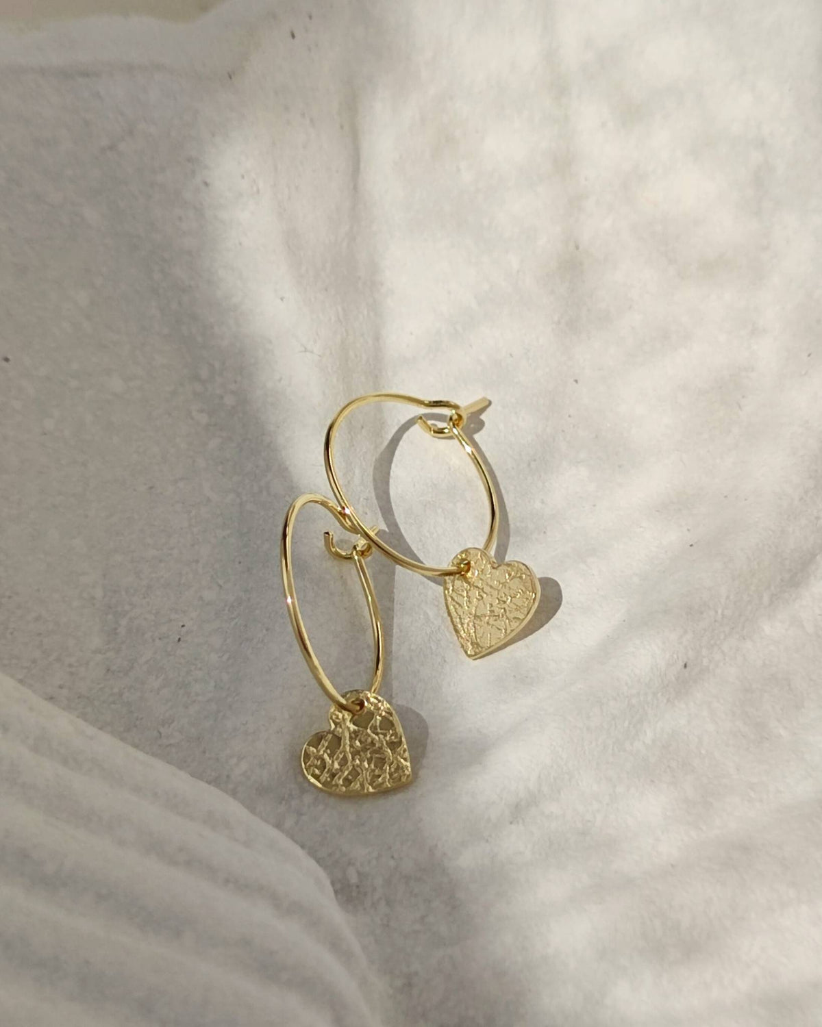 Dainty gold hoop earrings with small textured gold hearts lying on white ceramic dish