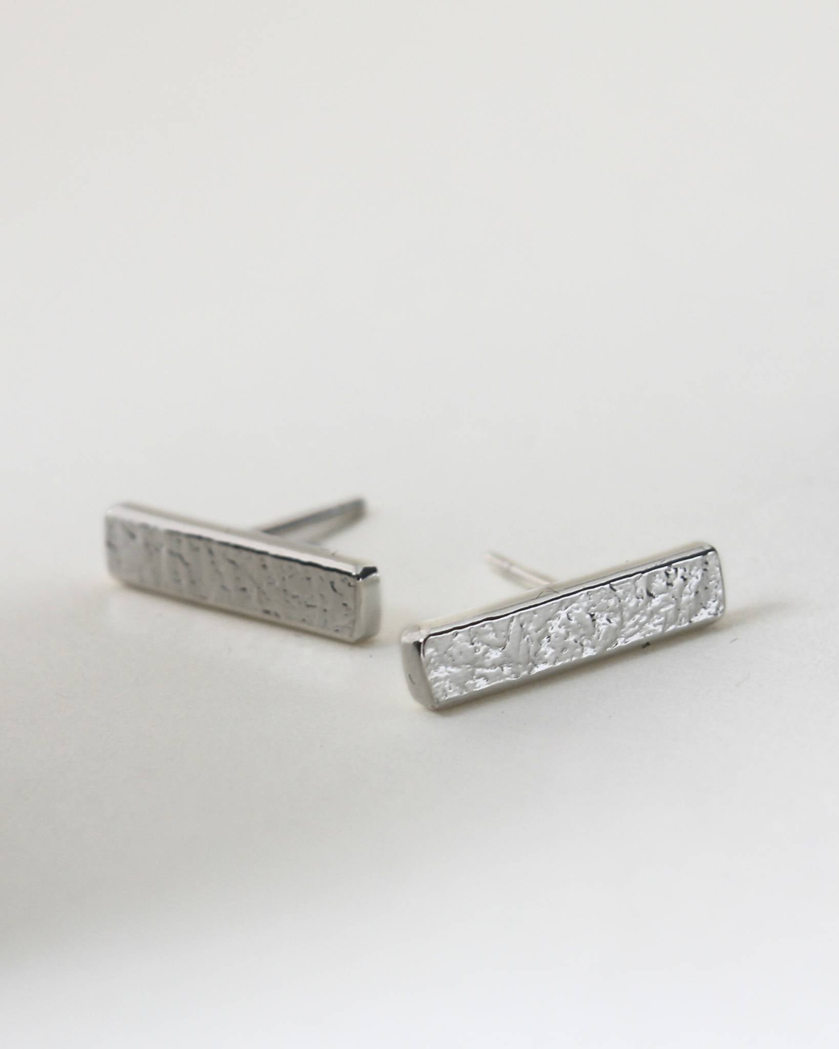 Silver rectangle bar stud earrings with textured surface on white background