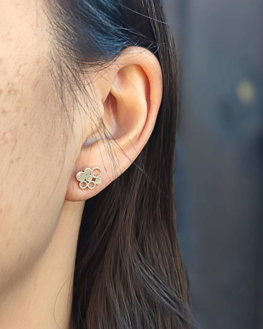 Close-up of an ear wearing a contemporary-style silver stud earring with a blurred background