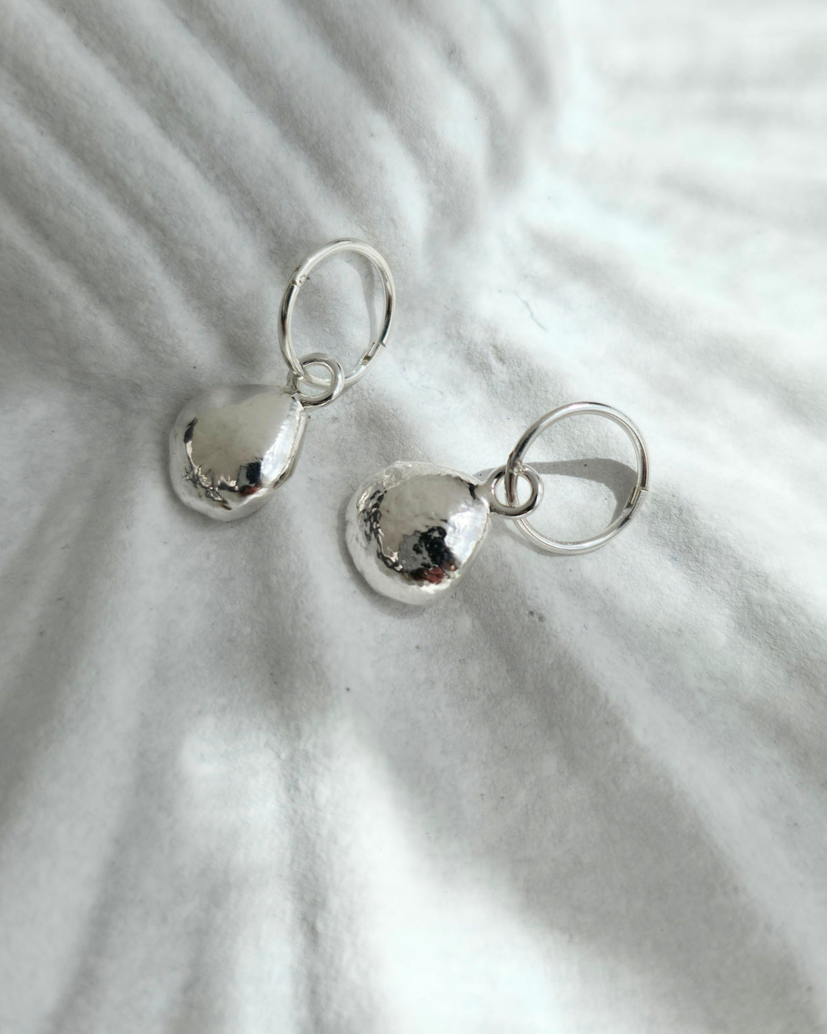 Pair of silver pebble-shaped earrings on a textured white surface
