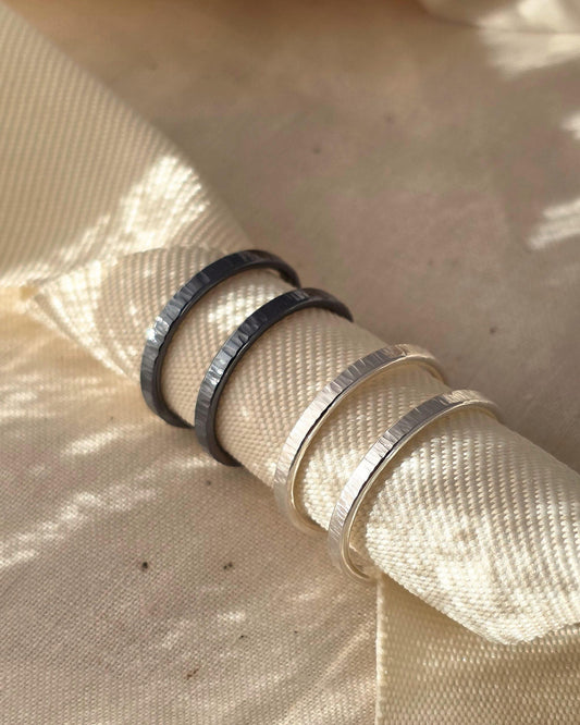 Handmade oxidised silver and sterling silver double band rings with hammered textures wrapped around thick beige ribbon and lying in sunshine
