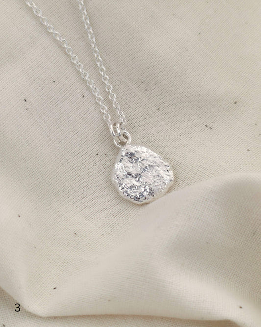 Sterling silver necklace with a textured round pendant on a beige fabric background