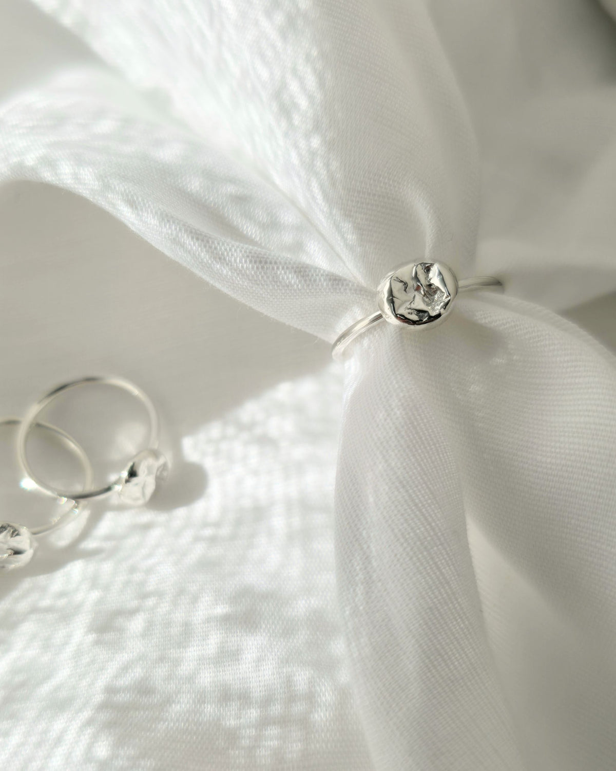 Three sterling silver rings with round textured molten nuggets lying on white fabric