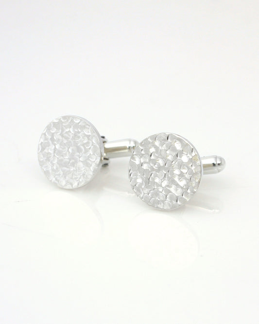 Silver circle cufflinks with reflective dimpled texture lying on white background