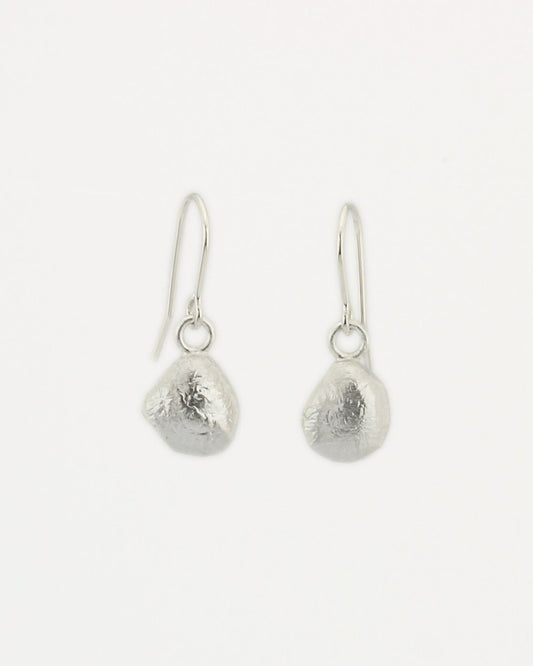 Teardrop-shaped molten silver earrings hanging from silver hooks with off-white background