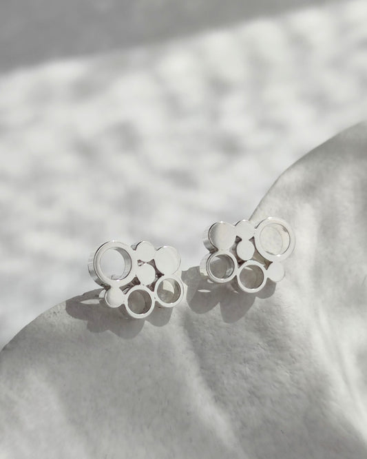 Sterling silver stud earrings with circle design lying in part shadow on white ceramic dish