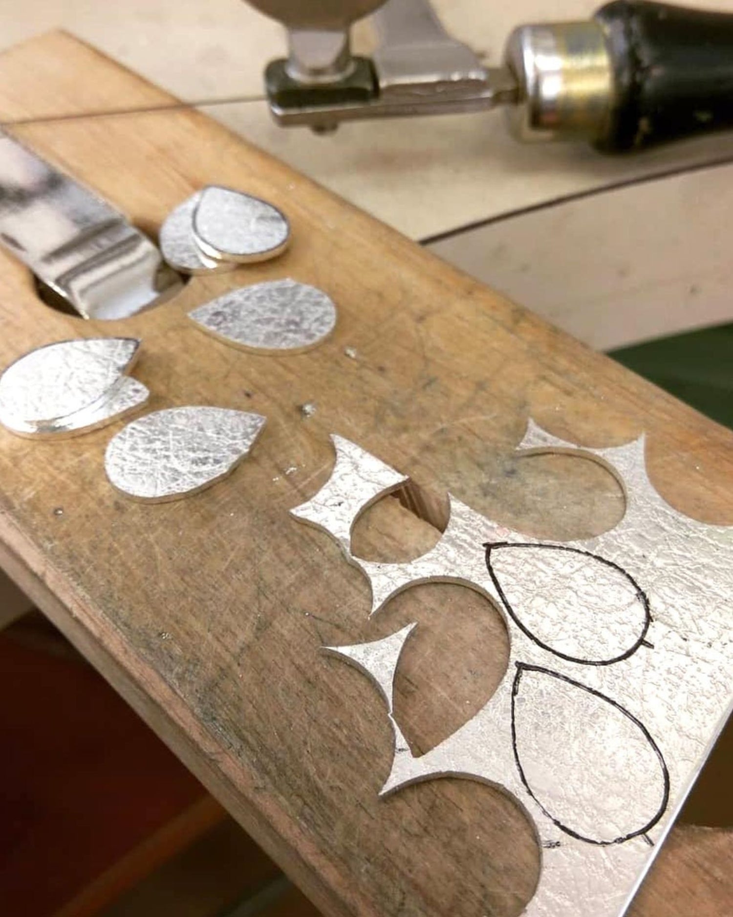 Piece of textured sterling silver plate with teardrop-shaped cut-outs on jewellers bench