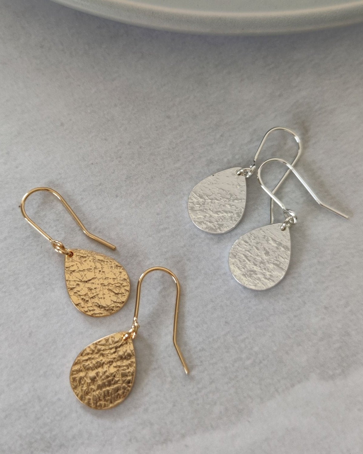 Gold and silver earrings with delicate textured surface lying on grey textured paper