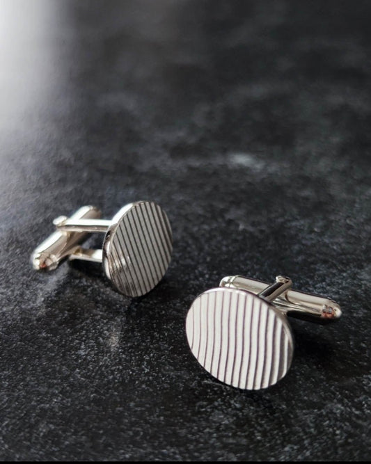 Sterling silver oval cufflinks imprinted with rippled texture lying on dark surface