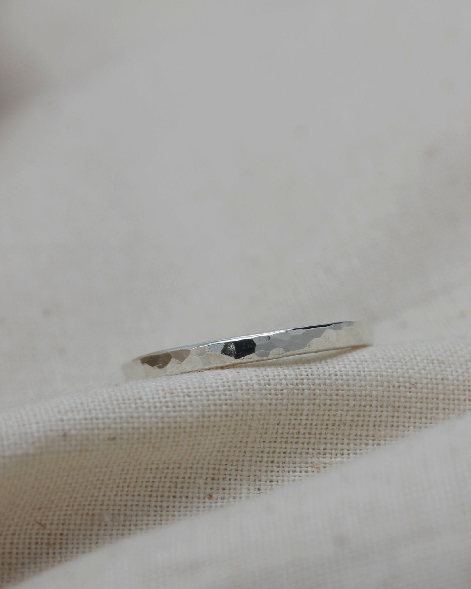 Delicate sterling silver stacking ring with hammered texture lying on beige fabric