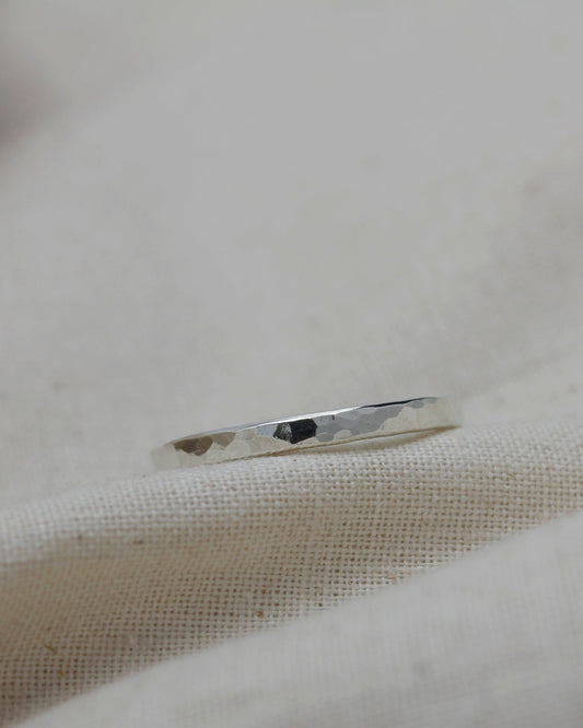 Delicate sterling silver stacking ring with hammered texture lying on beige fabric