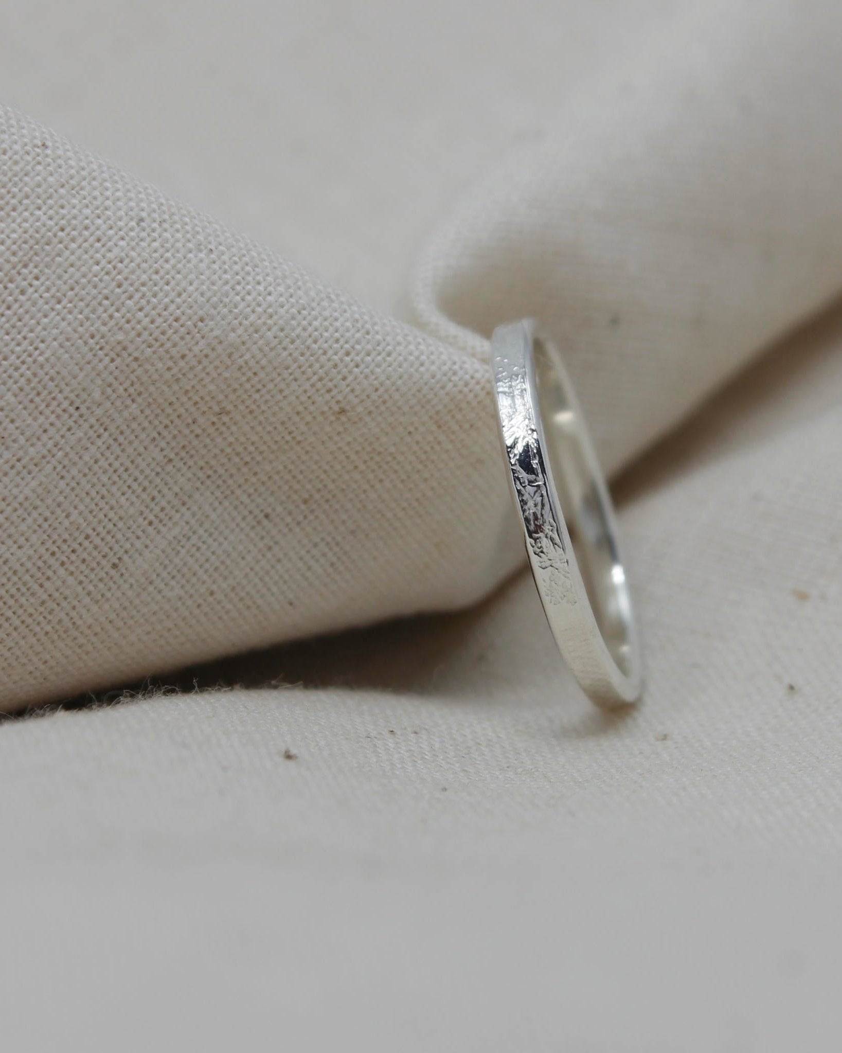 Dainty sterling silver stacking ring with textured surface lying against beige fabric