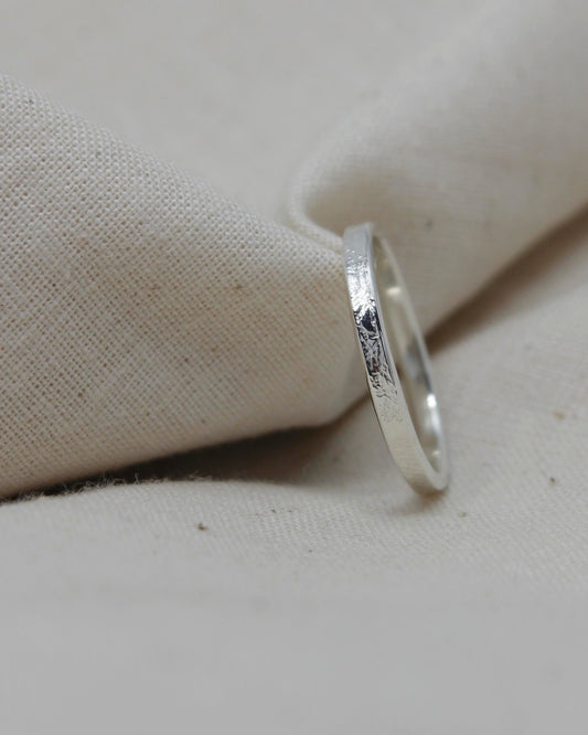 Dainty sterling silver stacking ring with textured surface lying against beige fabric