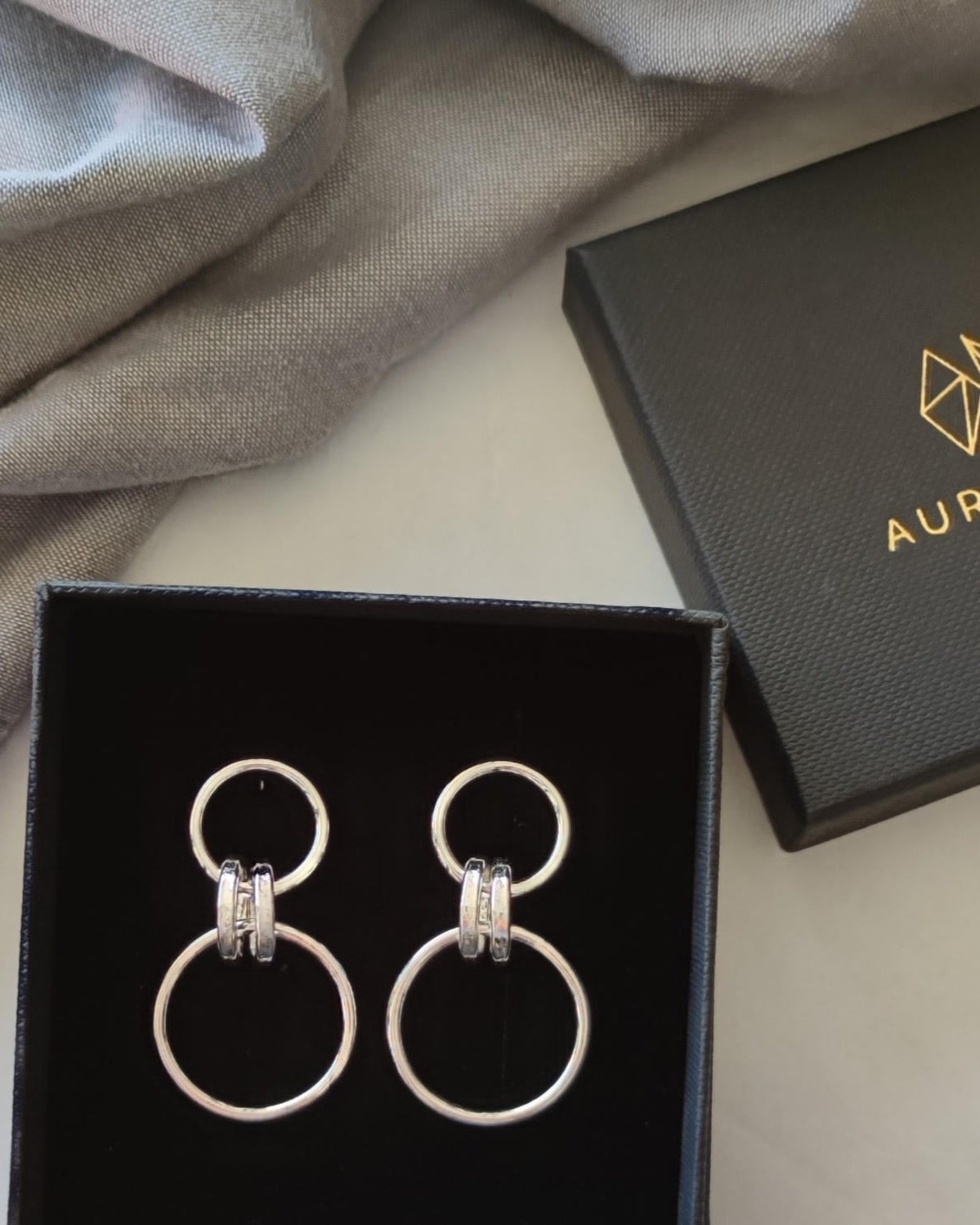 Handmade silver drop earrings made from small and large wire loops in black gift box beside grey fabric