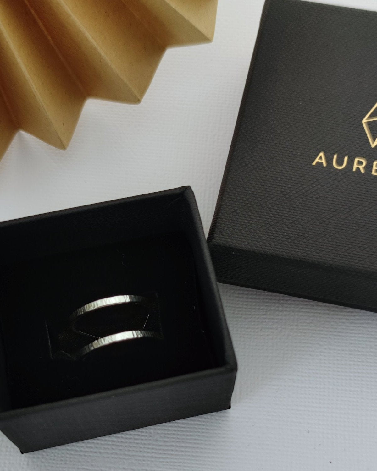 Minimalist silver double band ring in black gift box lying on white surface beside folded gold paper