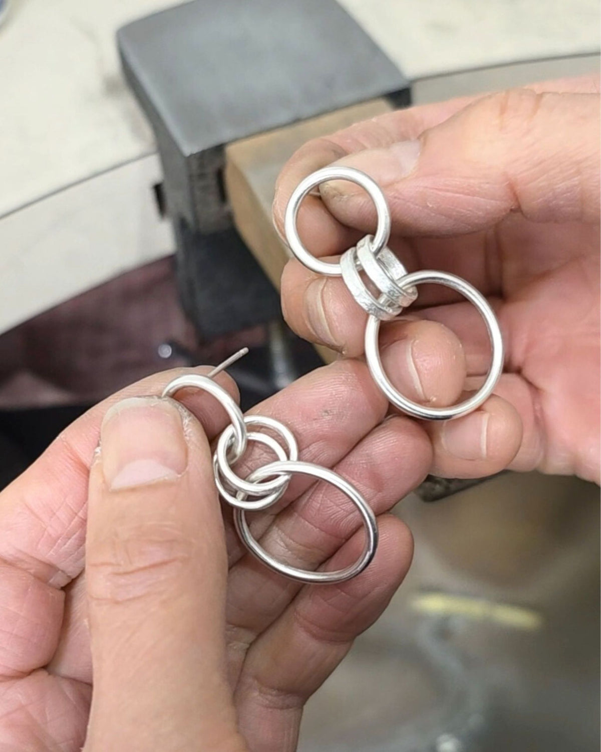 silver earrings with multiple loops held by hands on jewellery workbench