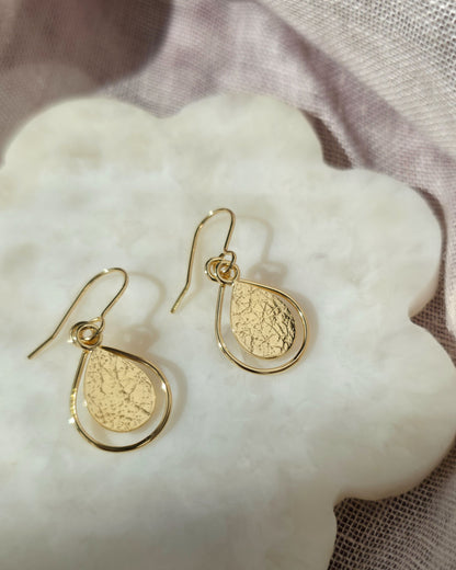Gold earrings with textured teardrop design on flower-shaped tile