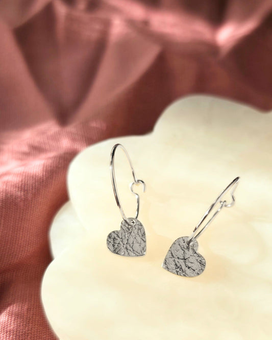 Silver heart-shaped earrings on a soft fabric background