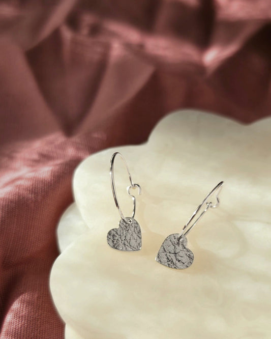 Silver heart-shaped earrings on a textured pink fabric background
