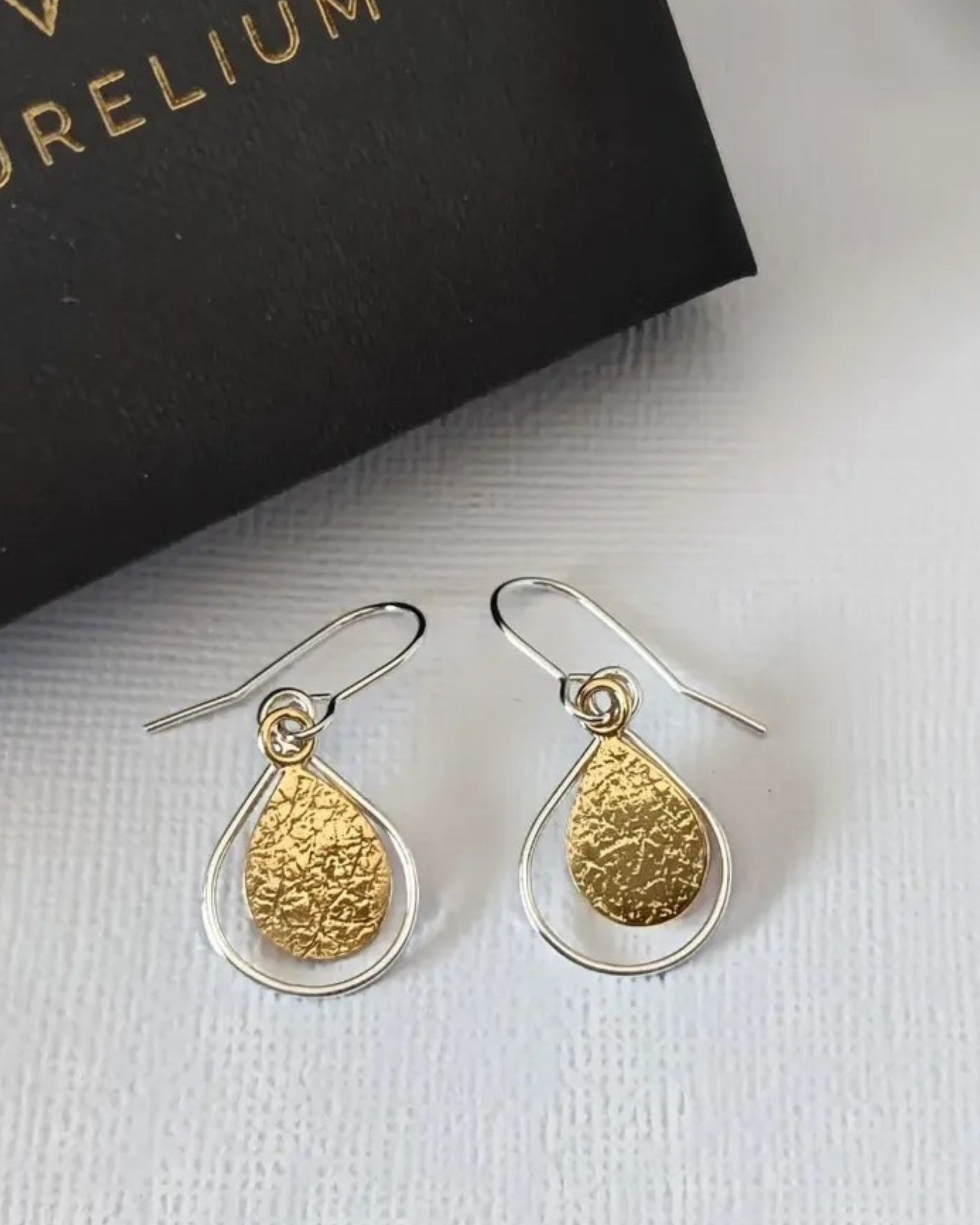 Gold and silver teardrop earrings on a white surface with a black box in the background