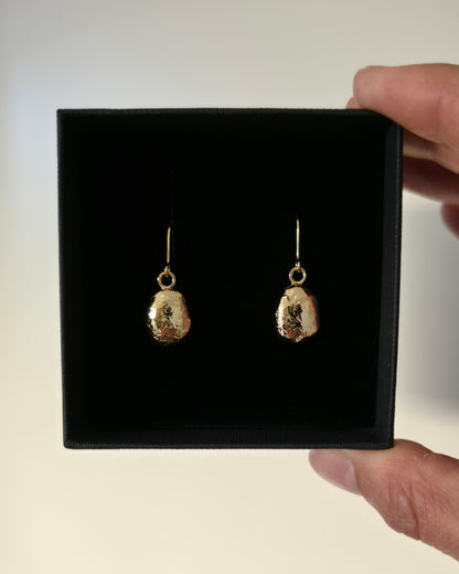 Hand holding a black jewellery gift box with gold oval earrings with a textured surface