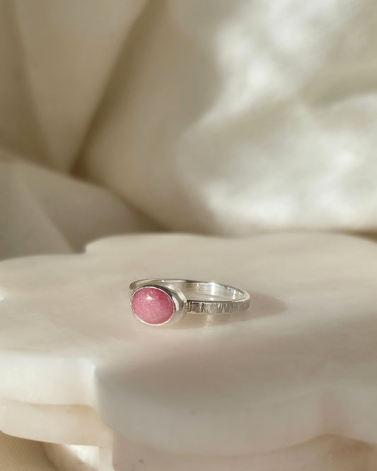 Silver ring with a blush pink stone on a soft white fabric background
