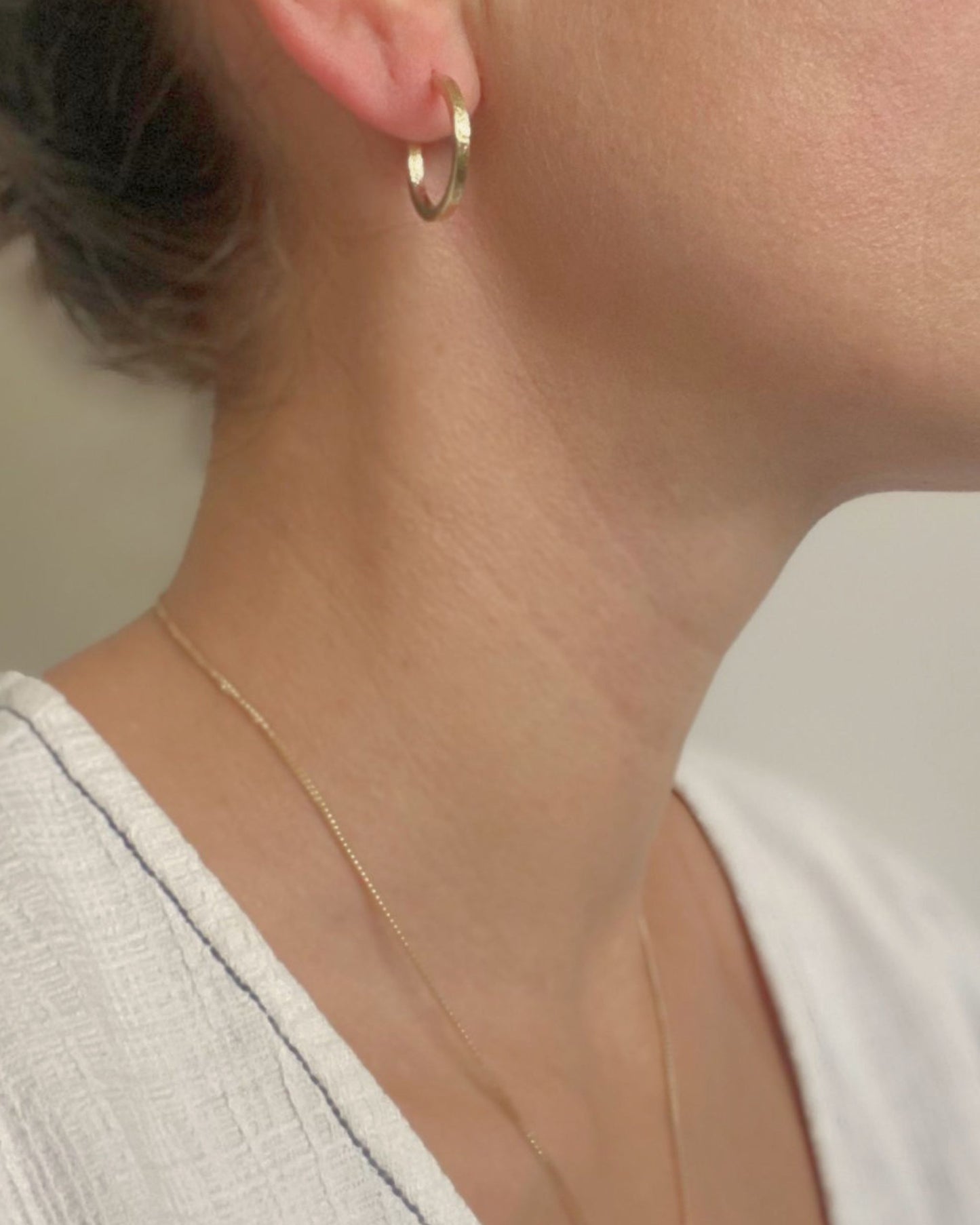 Close-up of a woman wearing a gold hoop earring and necklace