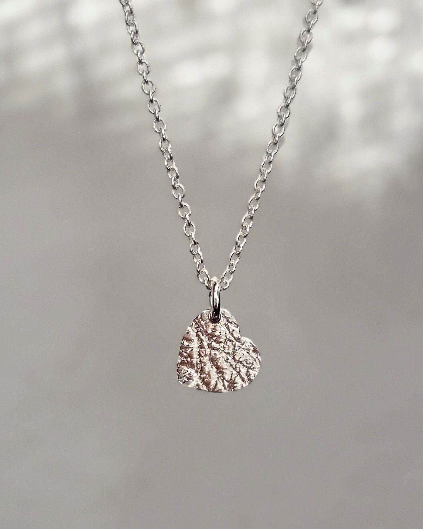 Sterling silver heart-shaped pendant necklace on a blurred natural background