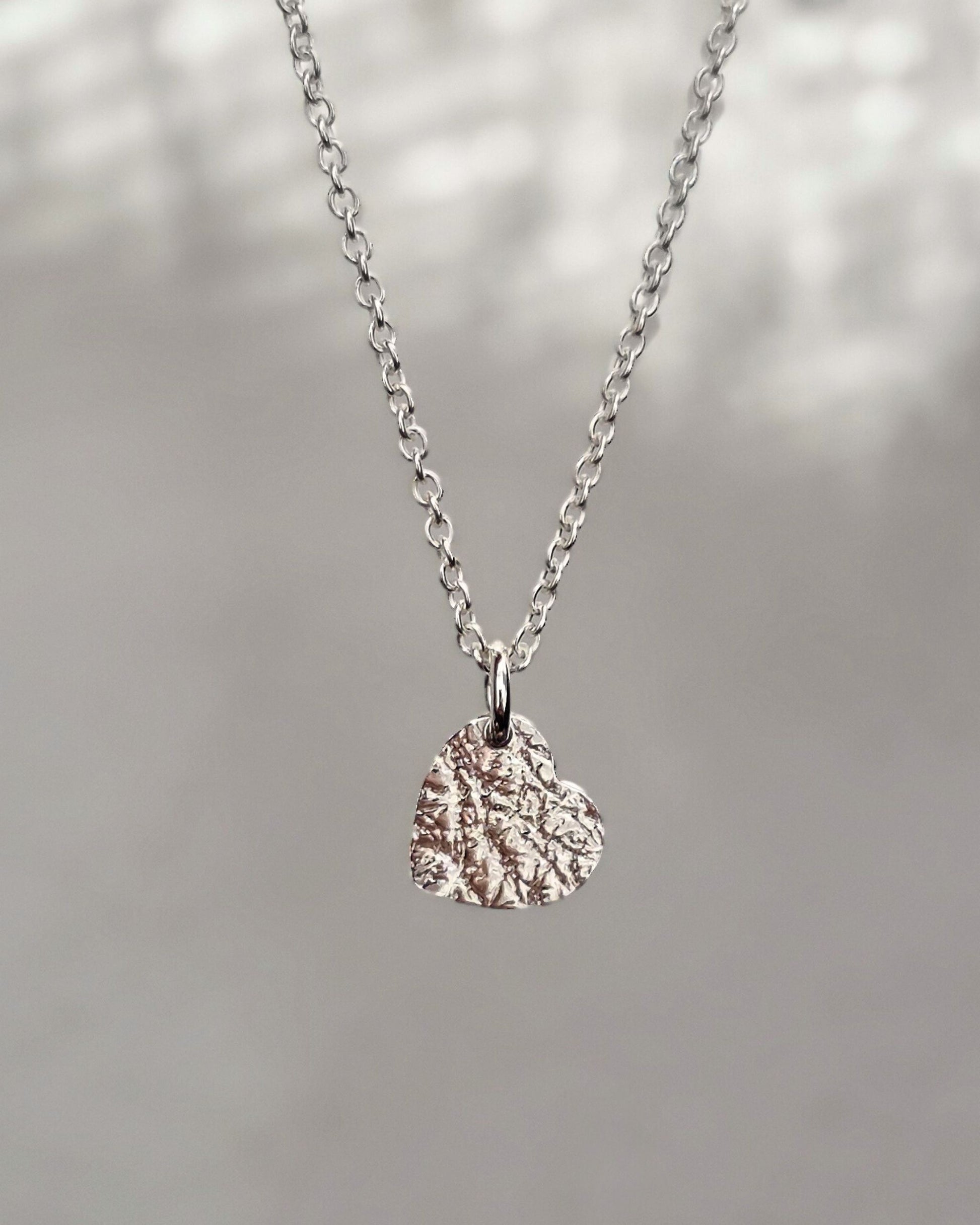 Sterling silver heart-shaped pendant necklace on a blurred natural background