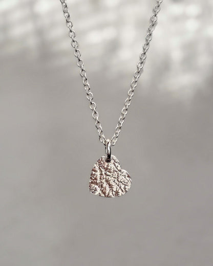 Sterling silver heart-shaped pendant necklace on a blurred natural background