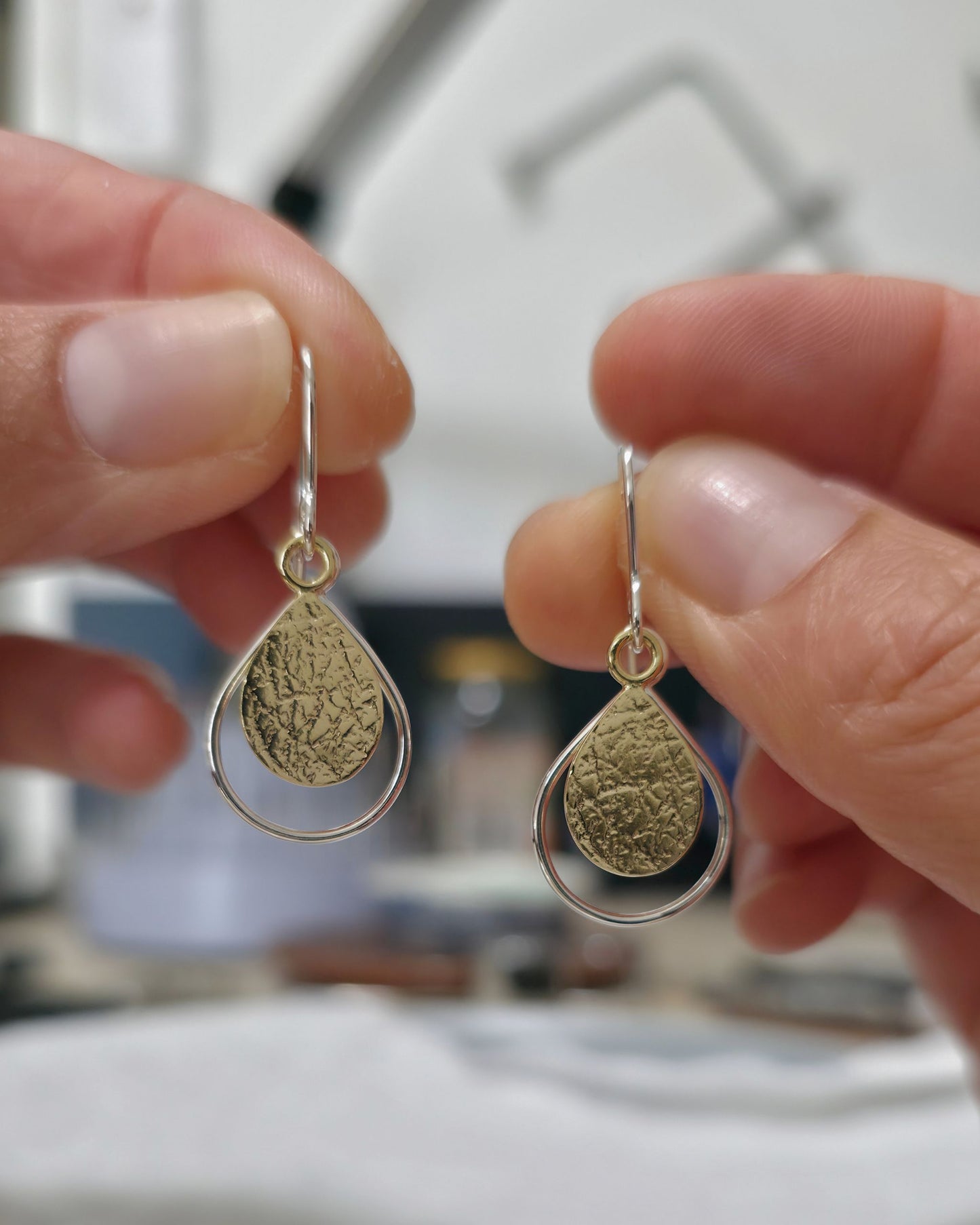 Textured gold teardrop earrings with silver wire borders held in fingers