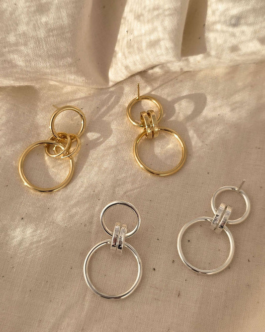 handmade gold and silver hoop earrings on a textured beige surface