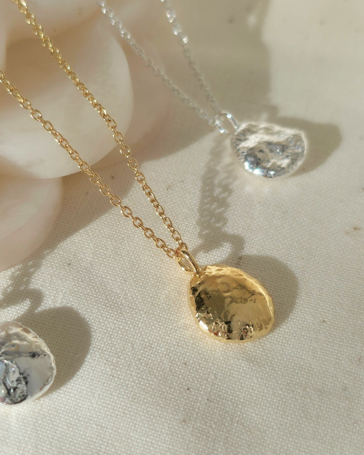 Gold and silver textured pendant necklaces displayed on a cream fabric background