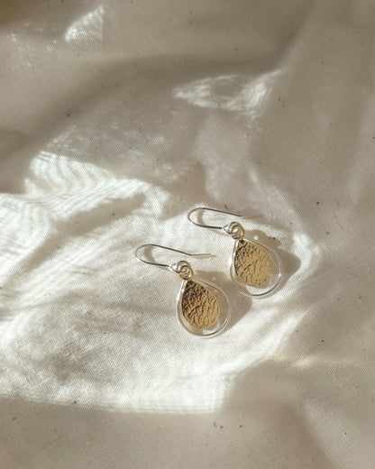Gold teardrop earrings with a silver wire teardrop border on a light fabric background