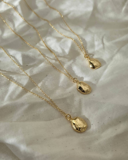 Three gold necklaces with textured oval pendants lying in the sun on a beige fabric background