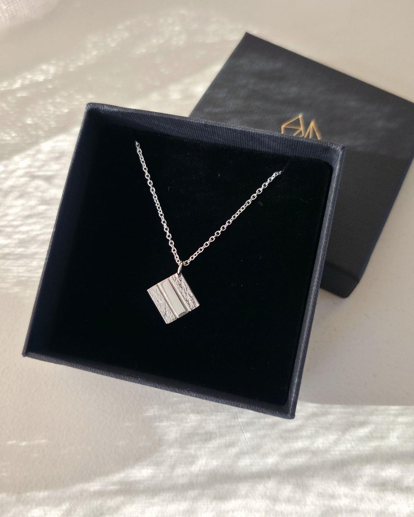 Silver necklace with a square pendant in a black jewellery box on a white background