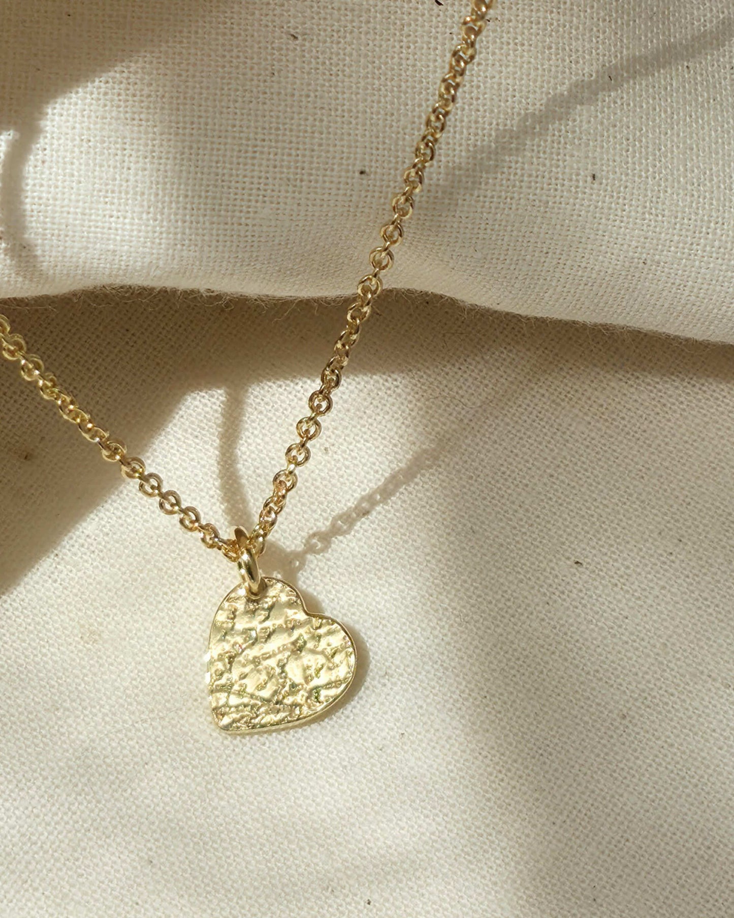 Gold textured heart-shaped pendant necklace on a beige fabric background