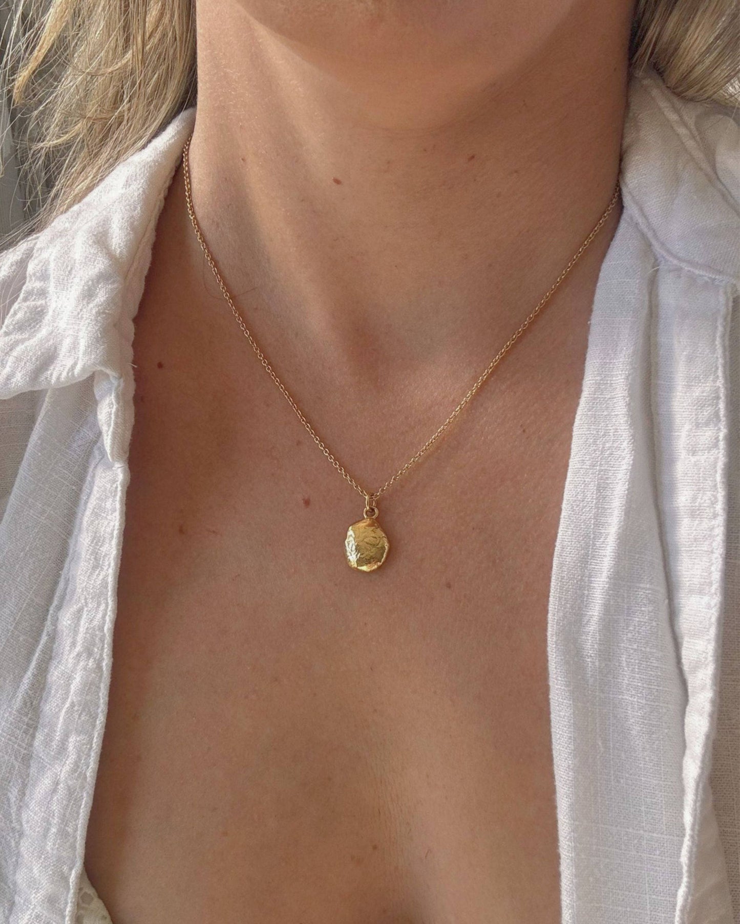 Person in a white shirt wearing a necklace with a small gold oval pendant