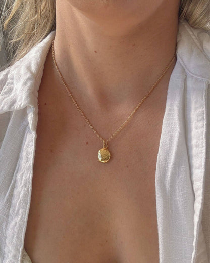 Person in a white shirt wearing a necklace with a small gold oval pendant
