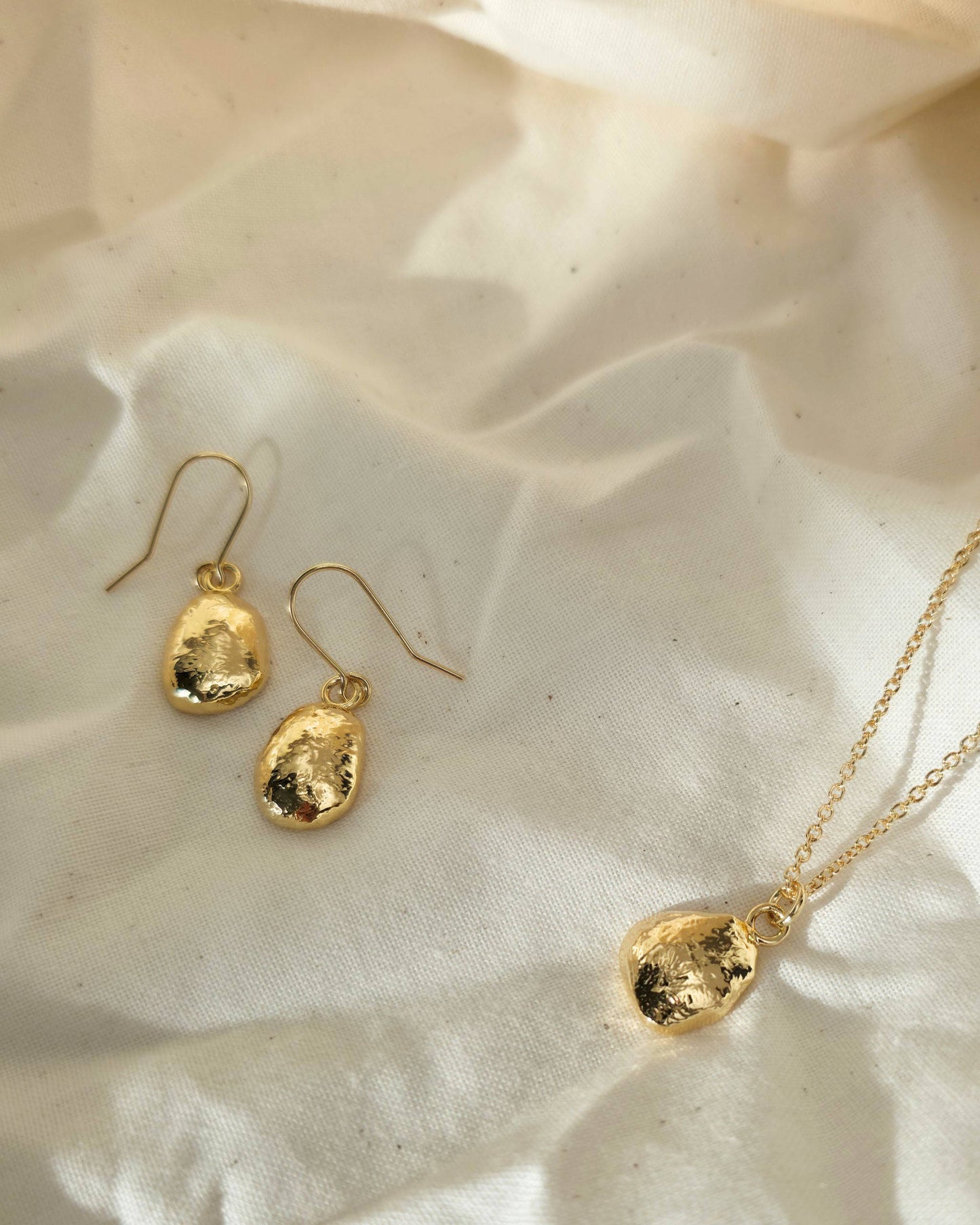 Gold oval shaped earrings and necklace on a beige surface